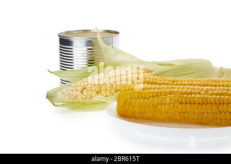 Fresh ripe ear of corn, plate with boiled corn on the cobs and canned corn in tin can on a white background. Stock Photo