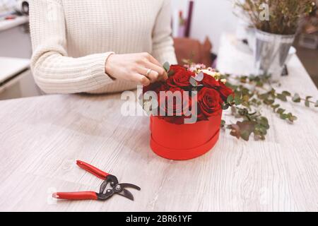 Flower shop florist woman making box with red roses. Process of creating hat-box with flowers Stock Photo