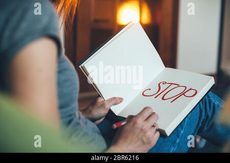Caucasian woman sitting on the couch and writing stop in the book with red pen Stock Photo