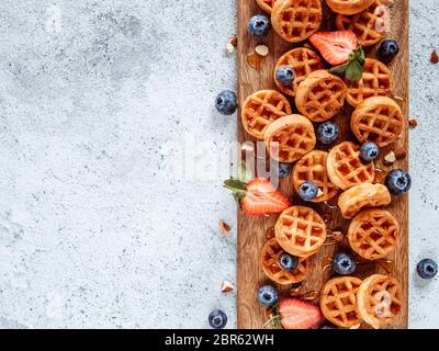Small round delicious soft belgian waffles on cutting board. Fresh belgian waffles with berries and caramel sauce top view. Copy space for text or moc Stock Photo