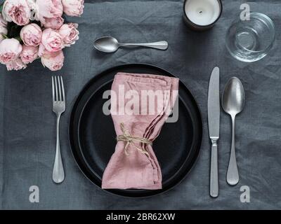Beautiful table setting with pink spray roses and candle on gray linen tablecloth. Festive table setting for wedding dinner with pink napkin on plate. Stock Photo