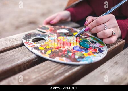 The artist who paints a picture in the park mixes paints on a palette Stock Photo