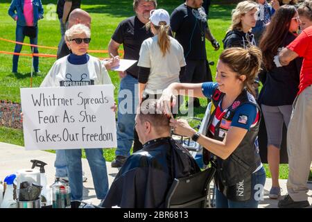 Lansing, Michigan, USA. 20th May, 2020. Barbers give free haircuts on the lawn of the Michigan State Capitol to protest Governor Gretchen Whitmer's emergency orders which keep many businesses closed during the coronavirus pandemic. The protest, called Operation Haircut, was organized by the Michigan Conservative Coalition. Credit: Jim West/Alamy Live News Stock Photo