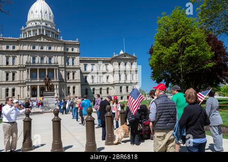 Lansing, Michigan, USA. 20th May, 2020. People line up as barbers give free haircuts on the lawn of the Michigan State Capitol. 'Operation Haircut' was a protest against Governor Gretchen Whitmer's emergency orders which keep many businesses closed during the coronavirus pandemic. The protest was organized by the Michigan Conservative Coalition. Credit: Jim West/Alamy Live News Stock Photo