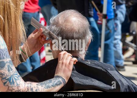 Lansing, Michigan, USA. 20th May, 2020. Barbers give free haircuts on the lawn of the Michigan State Capitol to protest Governor Gretchen Whitmer's emergency orders which keep many businesses closed during the coronavirus pandemic. The protest, called Operation Haircut, was organized by the Michigan Conservative Coalition. Credit: Jim West/Alamy Live News Stock Photo