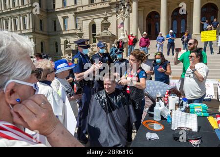 Lansing, Michigan, USA. 20th May, 2020. Barbers give free haircuts on the lawn of the Michigan State Capitol to protest Governor Gretchen Whitmer's emergency orders which keep many businesses closed during the coronavirus pandemic. The protest, called Operation Haircut, was organized by the Michigan Conservative Coalition. State police warned barbers that they were violating the law. Credit: Jim West/Alamy Live News Stock Photo