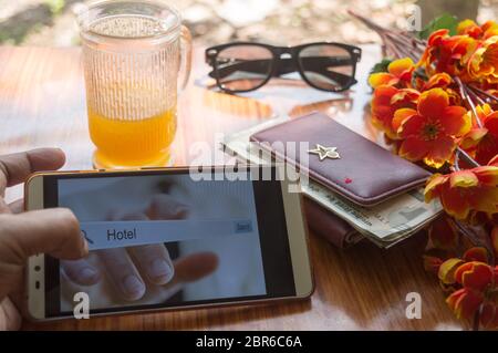 A business traveler search for reservation of holiday home. Close-up Of screen interface of booking hotels using cell phone along with travel accessor Stock Photo