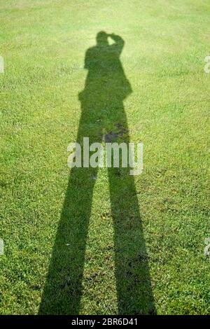 Shadow of a man on a background of green grass illustrates the concept of a photographer. Stock Photo