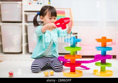 toddler girl play marble run game at home against white background Stock Photo