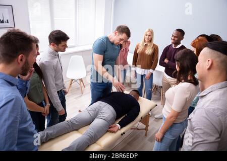 Male Instructor Teaching Massage Technique To Group Of Multi-ethnic People Stock Photo