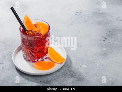Negroni cocktail in crystal glass in white ceramic plate with orange slice and black straw on light table background. Top view Stock Photo