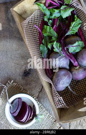 Bunch of fresh, spring, organic vegetables in a garden wooden box, with slices of beetroot in ceramic plate on old wooden background. Top view. Rustic, dramatic, organic kitchen. Ingredients, menu. Healthy life concept