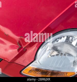 Scratches and rusty dent on front of red car, following an accident. Close-up. Stock Photo