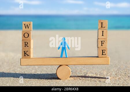 Blue Human Figure Standing Between The Work And Life Blocks Balancing On Seesaw At Beach Stock Photo