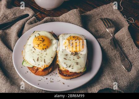 Italian toasts with vegetables and fried eggs on white plate and cup of coffee over grey rough cloth. Stock Photo