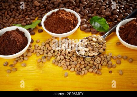 Gourmet coffee still life with assorted roasted and raw beans and freshly ground coffee in bowls over a stained yellow wood background with copy space Stock Photo