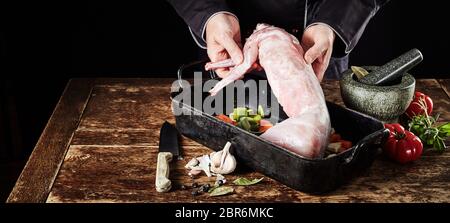 Chef preparing wild rabbit for a venison roast in a rustic kitchen surrounded by ingredients in a close up on his hands in panorama banner format Stock Photo