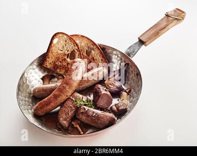 Assorted wild venison sausages with rye toast and herbs served in a copper pan high angle over white with copy spave Stock Photo
