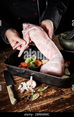 Chef preparing wild rabbit for roasting in a rustic kitchen displaying the cleaned skinned carcass to the view in a roasting pan with diced vegetables Stock Photo