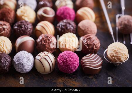 Selection of speciality handmade chocolate bonbons displayed on rustic wood with vintage wire fork and lifter with selective focus for advertising Stock Photo