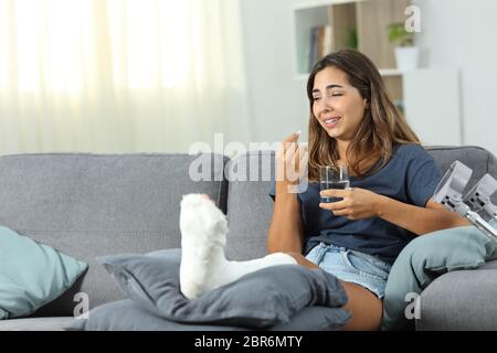 Disabled woman complaining crying taking pill sitting on a couch at home Stock Photo