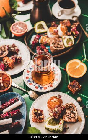 Variety of Turkish traditional lokum sweet delight with Turkish coffee in cups, tea in tulip glass and fresh fruits over green Moroccan tile table, to Stock Photo