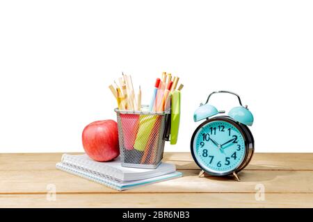 Pile of notebooks with apple and pencils in basket container with green stapler and alarm clock on wooden table isolated over white background. Back t Stock Photo