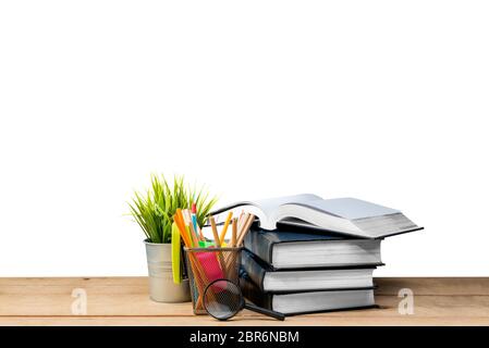 Pile of books with potted plant and pencils in basket container with magnifying glass on wooden table isolated over white background. Back to School c Stock Photo