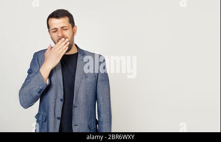 Business man on an isolated background bored yawns tired hand covering his mouth. Anxiety and drowsiness. A man lazily yawning early in the morning, wakes up and looks sleepy, tired and bored Stock Photo