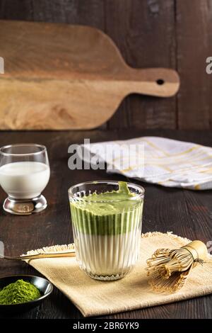 Matcha green tea latte, matcha powder and bamboo whisk on wood background.