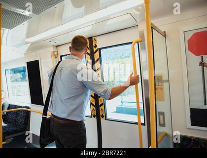A rear-view shot of a mid-adult businessman standing on a train commuting to work, he is arriving at his destination. Stock Photo
