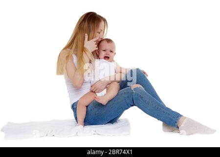 Young mother with unhappy crying baby  sit on a white background. Nursing and parenting. Eight months Stock Photo