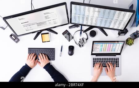 Elevated View Of Businesspeople's Hand Checking Invoice On Computer Over White Desk Stock Photo