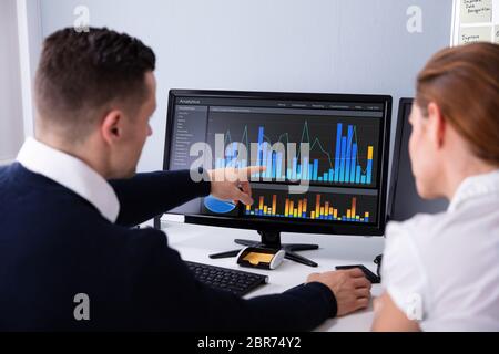 Side View Of Two Businesspeople Examining Graph On Computer At Workplace Stock Photo