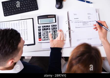 Elevated View Of Businesspeople's Hand Calculating Invoice With Calculator Over Desk Stock Photo