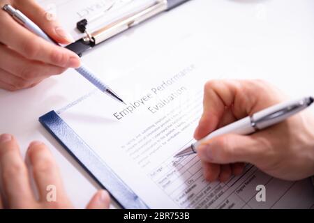 Close-up Of A Person Filling Performance Evaluation Form Of Employee Over Desk Stock Photo