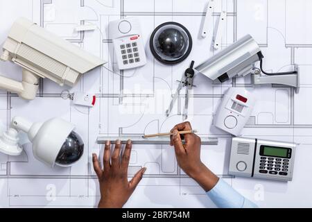 Close-up Of An Architect's Hand Drawing Blueprint Near Security Equipment Stock Photo