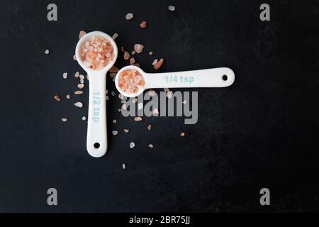 Pink Himalayan salt in measuring spoons on black background. Stock Photo