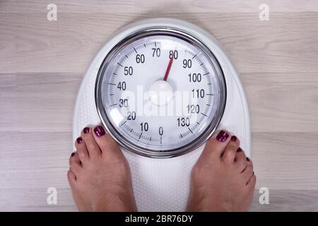 An Overhead View Of Woman's Foot On Weighting Scale Over The Hardwood Floor Stock Photo