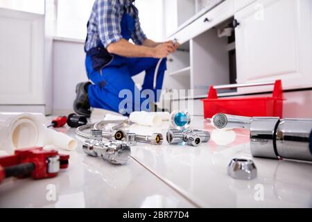 Plumber Tools And Equipment On Floor In Kitchen With Plumber Installing The Sink At Background Stock Photo