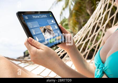 Young Woman Lying On Hammock Using Smart Home Automation On Digital Tablet At Beach Stock Photo