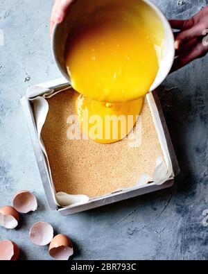 Lemon bar mixture poured from a hand held bowl into a paper lined baking tin. Stock Photo