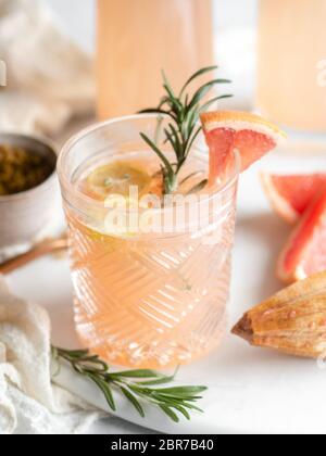 Old fashioned drinking glass filled with a grapefruit juice cocktail and garnished with lemon and rosemary on a blurred background Stock Photo