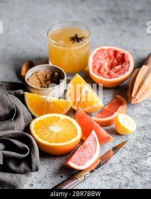 Sliced and halved oranges and grapefruits on a grey marble countertop, surrounded by a wooden hand juicer, a pocket knife, a grey napkin, a bowl of br Stock Photo