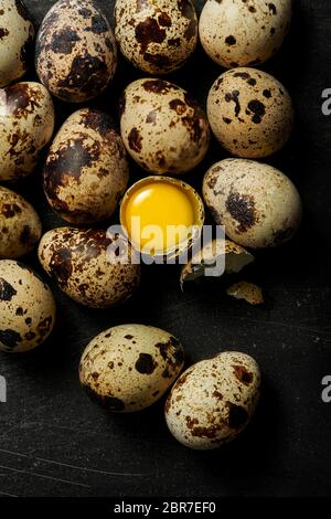 Quail eggs on a black rustic surface with one cracked open to show raw yolk inside. Stock Photo