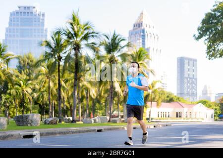 Asian young man are jogging and exciseing outdoor in city park and wearing protective mask on face for stay in fit during Covid-19 pandemic in Bangkok Stock Photo