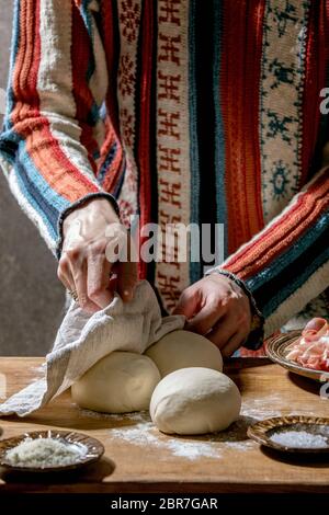 Woman in knitted sweater cooking italian pizza napolitana. Three balls of fresh homemade wheat dough, prosciutto and ingredients in ceramic plates abo Stock Photo