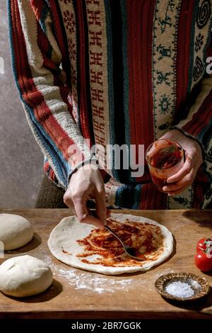 Woman in knitted sweater cooking italian pizza napolitana. spread fresh homemade wheat dough with tomato sauce. Ingredients in ceramic plates above on Stock Photo