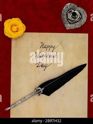 Antique preachment with hand written Happy Valentines Day, yellow rose, detailed silver quill stand in shape of hart accented by flat lying beautifull Stock Photo