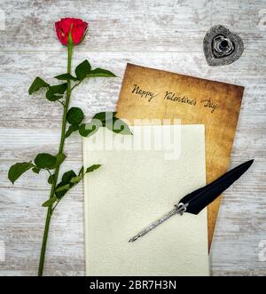 Antique preachment with hand written Happy Valentines Day, sticking out from book, red rose, detailed silver quill stand in shape of hart, ornamented Stock Photo
